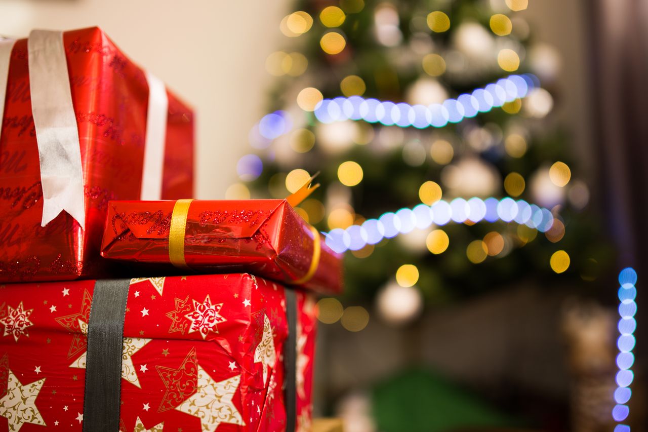 Christmas presents in red wrapping with a glowing bokeh tree background, emphasizing holiday spirit.