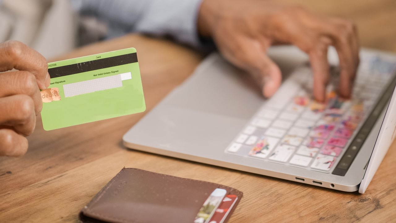 About Person using a credit card for an online purchase on a laptop at a wooden table.